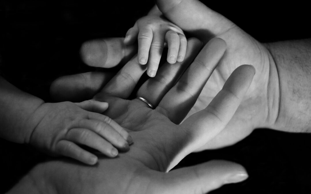 Black and white image of a baby's tiny fingers grasping the hands of their parents, symbolizing the foundation of love, faith, and connection in a Christ-centered home.